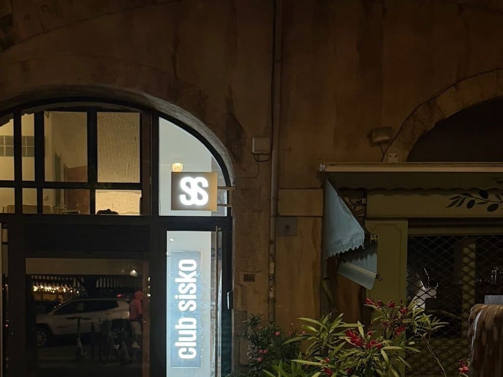 Devanture du Club Sisko au 14 place aux Huiles à Marseille, de nuit, arche en pierre et enseigne lumineuse au monogramme