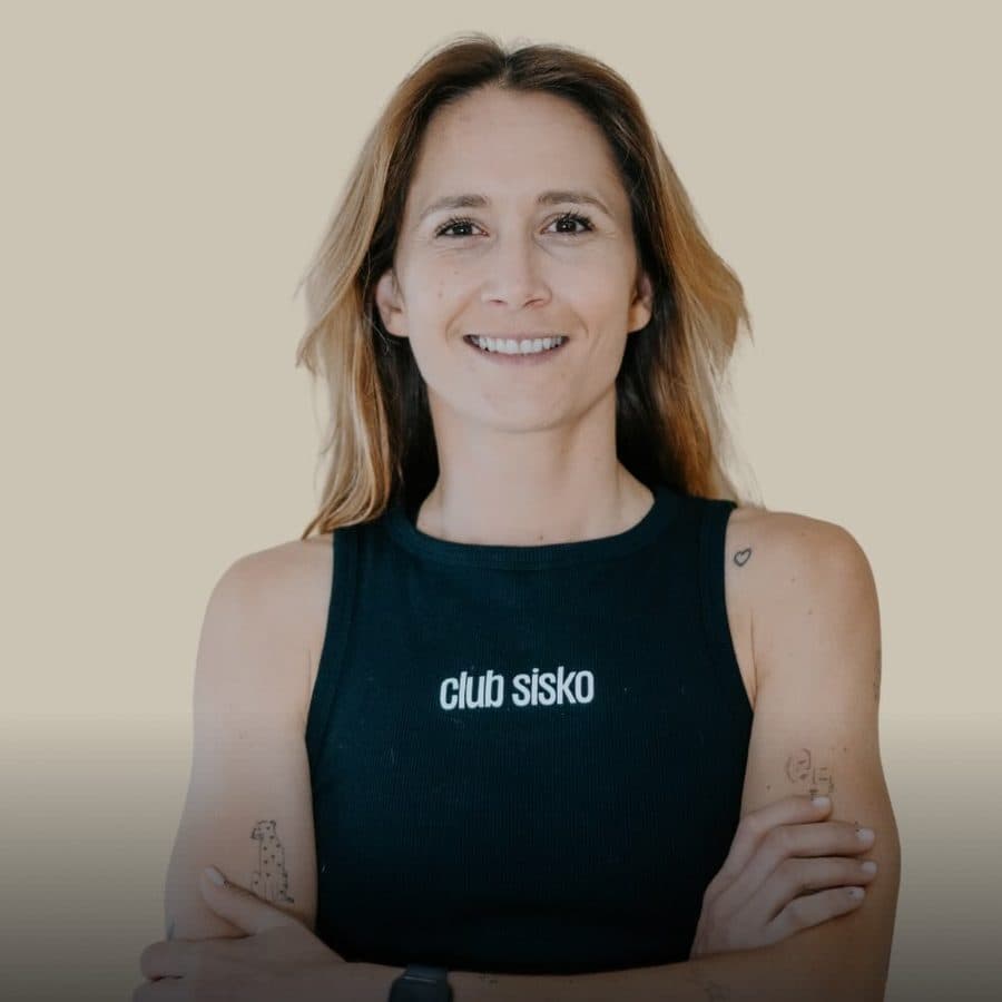 Merryl, coach et cofondatrice du Club Sisko, souriante et bras croisés en débardeur noir sur fond beige