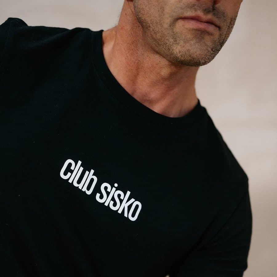 Homme en t-shirt noir Club Sisko, haltère en main, plan serré sur fond beige, visuel Bootcamp BodySculpt