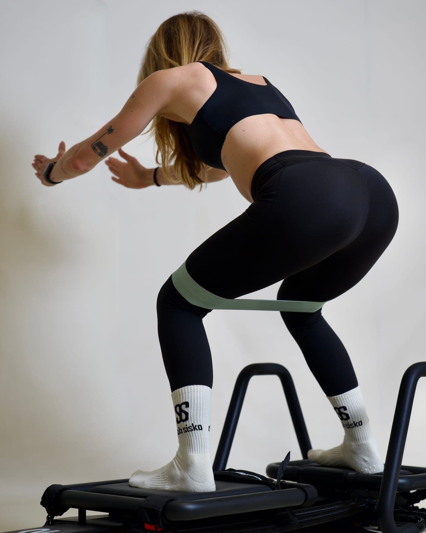 Pratiquante en squat sur Microformer, élastique au-dessus des genoux et chaussettes Club Sisko, pendant un exercice de Lagree